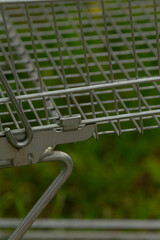 Abandoned shopping icon near natural park, Metal container beneath grass with contrasting wire legs and lighting, Underside of metal basket over grass showing wire framework and nearby park pathway