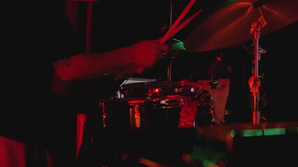 A drummer plays the kit. His hands move as he plays the snare drum. Side view. The scene is vibrant with color, emphasizing the drummer's focus and passion for the music