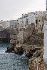 dramatic view of polignano a mare, puglia, italy, showing the iconic white architecture perched precariously on rugged limestone cliffs above the adriatic sea