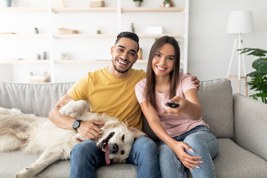 A young couple enjoys a relaxing evening on their couch with a friendly dog. They are watching TV together, creating a cozy and joyful atmosphere in their home. - Powered by Adobe