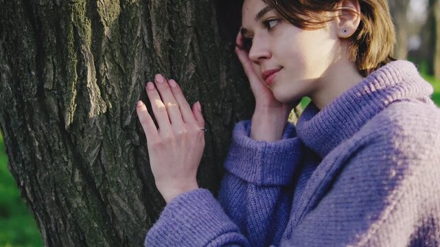 Woman leans against a tree while resting her head on her hand in a green setting during daytime