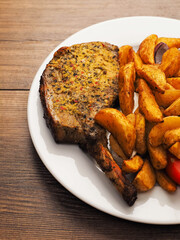 Fine dinner with spicy pork chop, potato wedges and fresh tomato on a plate on a wooden table. Tasty meal with meat and vegetables.