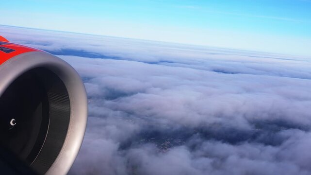 Aerial window view shows a large turbofan left foreground as the plane passes over clouds near Funchal, Madeira, with contrails and lights visible in bright daylight.