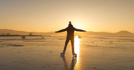 LENS FLARE, SILHOUETTE: Female skater glides gracefully on frozen Lake Cerknica during winter...
