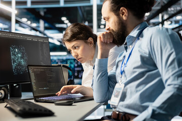Team of programmers using notebook in server room, analyzing data. Data center office IT experts doing brainstorming, examining code on laptop, ensuring system integrity and security