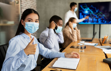 In a contemporary office, diverse business professionals engage in a corporate meeting while wearing medical masks.