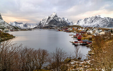 Panorama view of the village of Reine, a famous fishing village located in front of snow-covered mountain range, under sunset