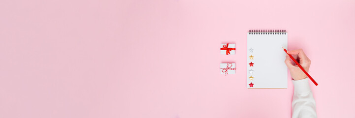 Holiday banner with female hand writing in blank notebook, Christmas gifts and glitter stars on pink copy space for planners, checklists, marketing designs and festive social media content