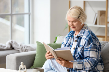Senior woman reading book on sofa at home