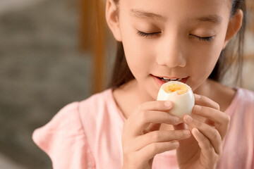 Cute Asian girl eating boiled egg in kitchen, closeup