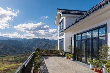 Fototapeta premium This contemporary house boasts a spacious balcony that offers stunning views of the surrounding mountains during the day, complete with fluffy clouds in the blue sky and lush greenery in the landscape
