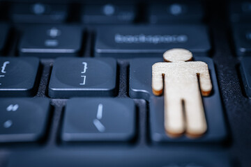 Wooden figure of a man placed on a black computer keyboard, symbolizing technology and human interaction in a digital workspace