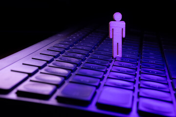Wooden figure standing on a laptop keyboard illuminated with purple light, symbolizing technology and digital connection in a modern workspace