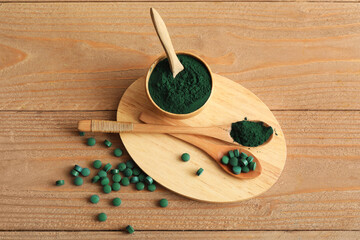 Bowl of spirulina powder with spoons and capsules on wooden background