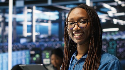 Portrait of smiling server room engineer using device to interpret AI generated data analytics graphs. Happy data center worker using artificial intelligence tool showing system metrics, camera B