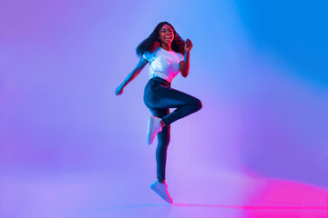 A young woman with long hair is energetically dancing with a smile, wearing a white top and jeans. The colorful backdrop creates a vibrant atmosphere in the studio.