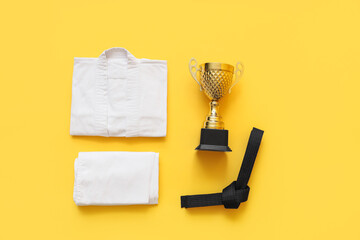 Karate uniform with black belt and gold cup on yellow background