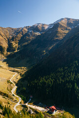 Picturesque alpine valley with tiny houses, curved mountain road and forest slopes under clear sky at Transfagarasan Highway in Romania