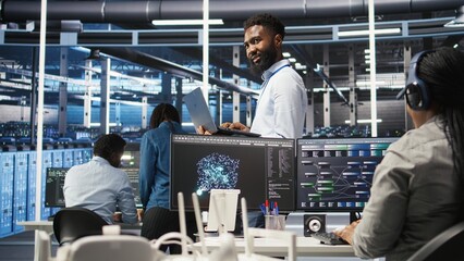 Happy data center admin uses node tree programming on laptop to identify equipment performance issues. Cheerful server farm worker reviews data analysis graph to minimize hardware failures, camera A