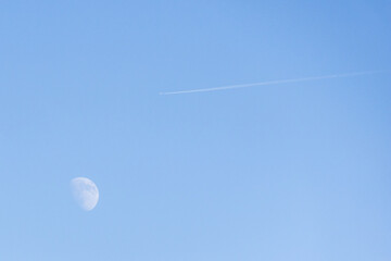 Moon and airplane contrail crossing a blue sky