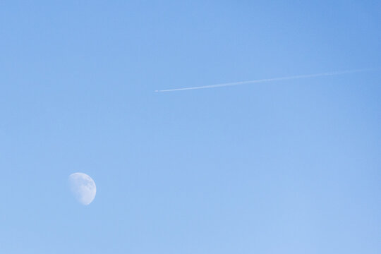 Moon and airplane contrail crossing a blue sky - Powered by Adobe