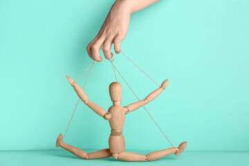 Hand of puppeteer manipulating marionette on turquoise background