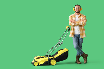 Young man in hearing protectors with lawn mower on green background