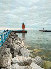 Red lighthouse at the end of the pier on the water with a rocky shoreline. Located on Round Lake which leads to Lake Michigan in Charlevoix, Michigan, USA. Charlevoix South Pier Light Station.