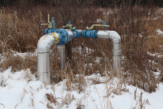 A pipeline backflow prevention valve. Three pipelines coming together into one set of valves. Set in an outdoor treed wild area.
