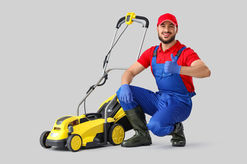 Male gardener with lawn mower showing thumb-up on light background