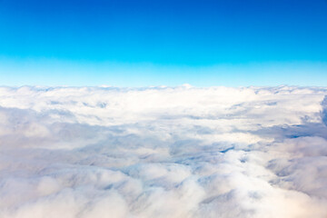 Aerial view of dense fluffy white clouds under a clear blue sky.