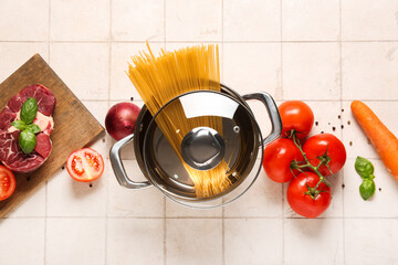 Cooking pot with different vegetables, pasta and beef on white tile background