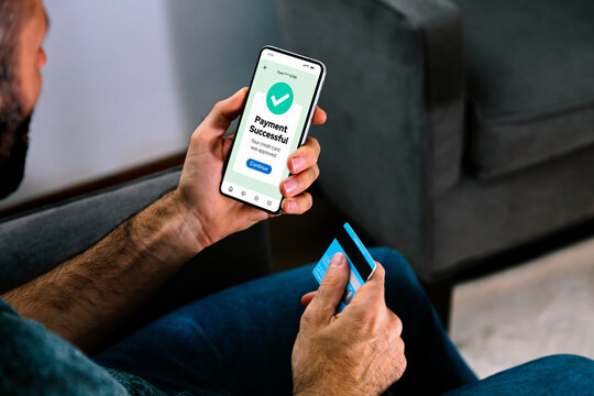Making a credit or debit card payment online. Successful digital payment confirmation on a mobile phone screen. Man in his living room completing a purchase.
