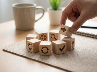 Continuous improvement cycle and showing cubes arranged in an endless loop using wooden cubes, symbolic icons, human hand, natural depth of field, soft blurred background, minimal desk background