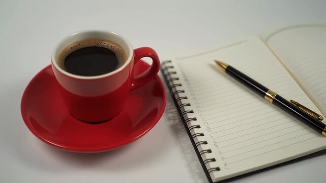 High-quality footage showcasing a red cup of black coffee, an open notebook, and a pen. Perfect for work, study, creative, or thoughtful break scenes, symbolizing focus and inspiration