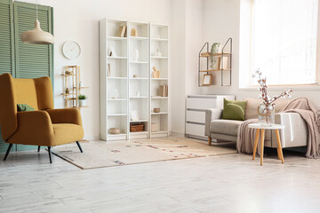 Interior of living room with sofa, armchair, shelving units, folding screen and cotton flowers in vase on table