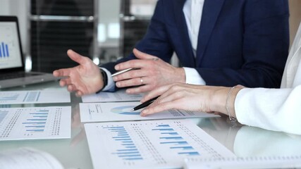 Business professionals collaborating in a modern office, reviewing financial reports, charts and a laptop on a glass table while discussing data analytics, strategy and planning - Powered by Adobe