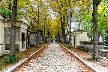 Glimpse of tree-lined avenue with cobblestones in the monumental Cemetery of Pere Lachaise, largest cemetery in Paris, France, where many famous artists are buried.
