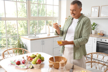 Mature man with honey making apple cider at table in kitchen