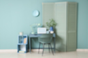 Blurred view of living room with comfortable workplace, folding screen and shelving unit near mint wall
