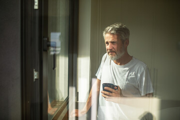Mature man drinking coffee, pensive by home window