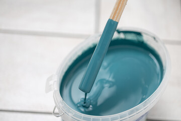 Paint bucket filled with vibrant teal paint and a brush, showcasing rich texture and color, ideal for artistic projects and home decor