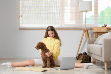Sporty teenage girl with Poodle dog and laptop training at home