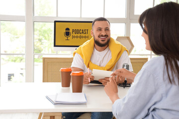Male podcaster with notebook and woman at table in studio