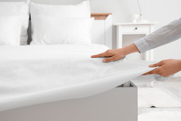 Female hands putting white blanket on bed in room, closeup