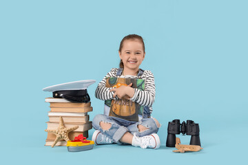 Fototapeta premium Cute little girl with adventure books and toys sitting on blue background