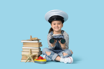 Fototapeta premium Cute little girl in pilot's hat with binoculars and adventure books on blue background