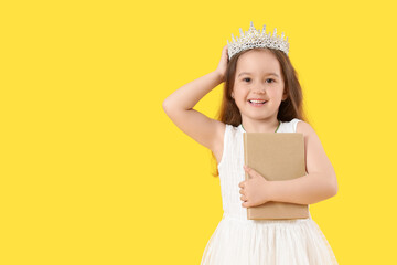 Cute little girl in tiara with adventure book on yellow background