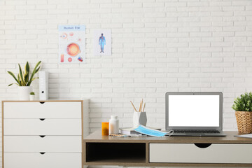 Blank laptop with doctor's supplies on desk in medical office