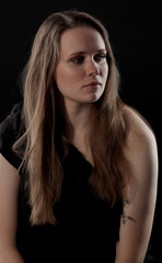 Fototapeta premium Studio portrait of a young woman with long blonde hair against a black background. This image is suitable for fashion beauty and editorial projects.